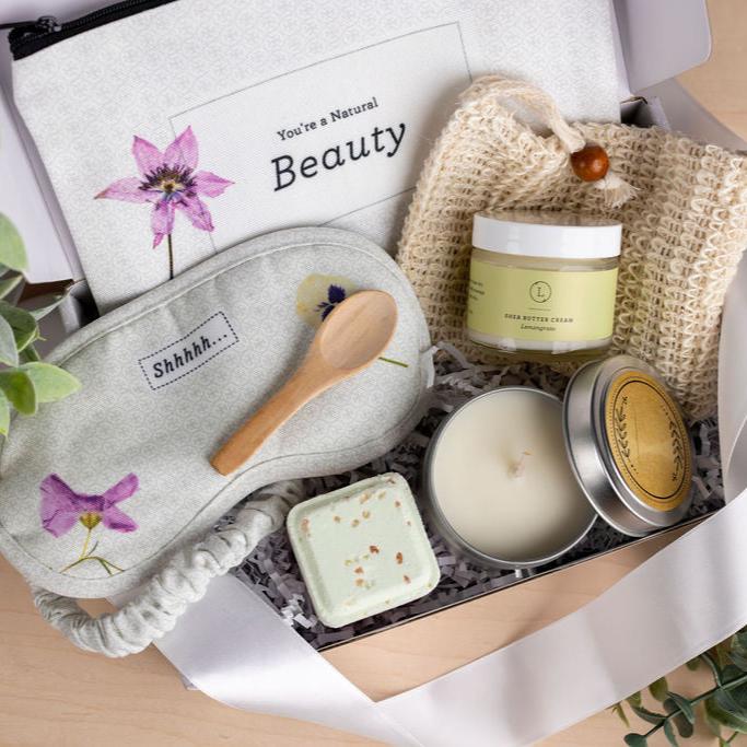 Self-Care Package displayed as a care set, featuring soothing and luxurious items perfect for pampering. The set includes a scented candle, shea butter infused with essential oils, a shower steamer, a shower steamer saver, an eye mask, and a cosmetic bag. All items are arranged in a beautiful large gift box, with an option to personalize the lid with the recipient’s name for an extra special touch. This thoughtful package is ideal for any occasion and can be customized with a personal gift message during ch