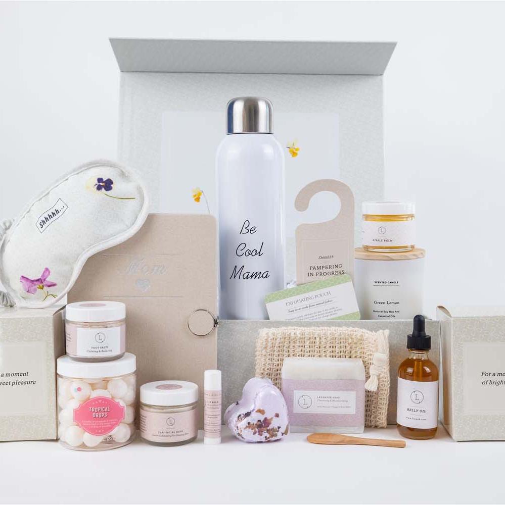 New mother gift box thoughtfully curated to bring joy and comfort before and after the baby arrives. The set includes essentials like nipple balm, belly oil, a 'Be Cool Mama' water bottle, a scented candle, a 'Mom' journal with a heart symbol, lavender natural soap, lavender foot salt, candy sparkle, a heart-shaped shower steamer, a facial clay mask, unscented lip balm, a cotton eye mask, a natural luffa soap saver, and a door hangtag.