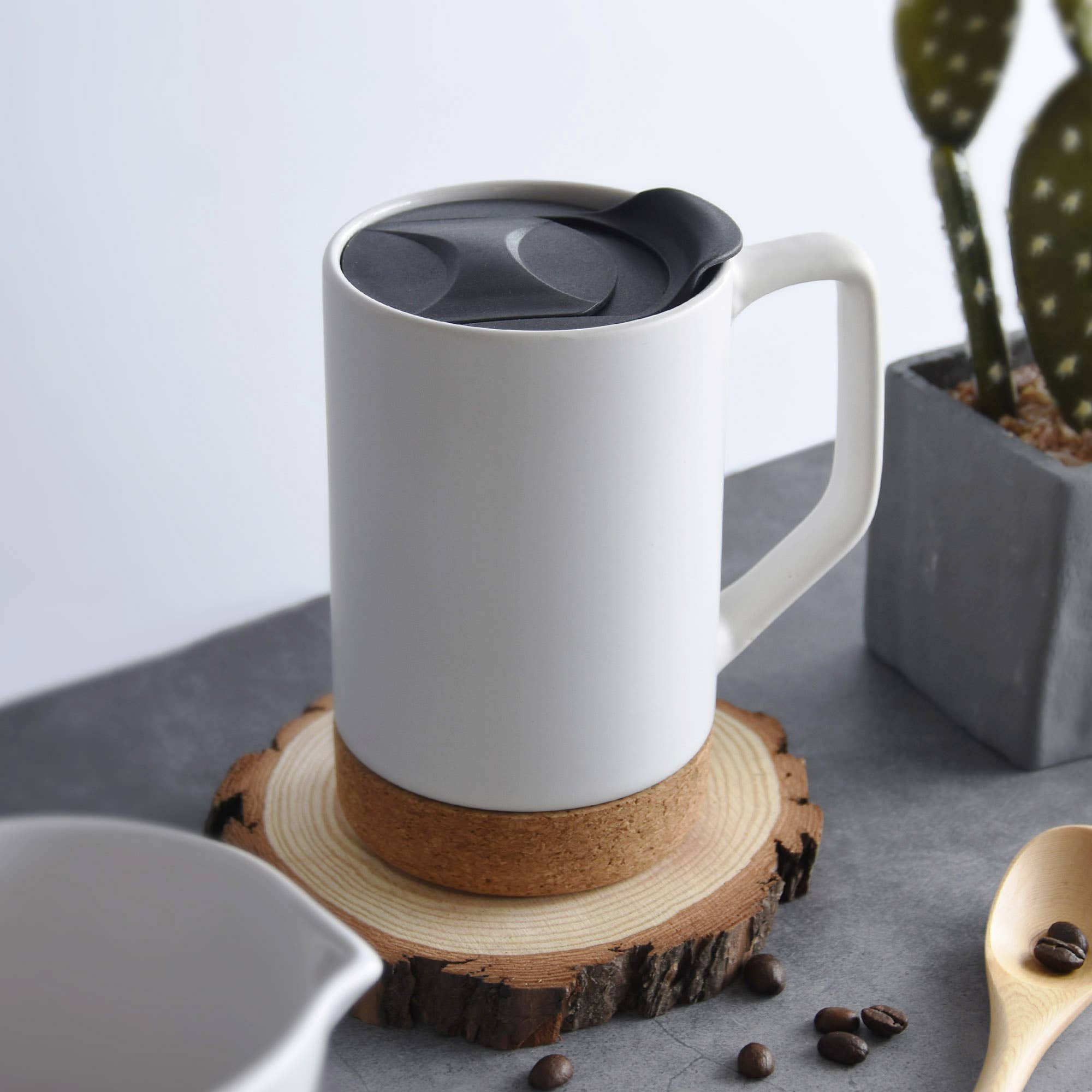 A matte white ceramic coffee mug equipped with a splash-proof lid and a comfortable large handle, displayed on a light marble countertop.